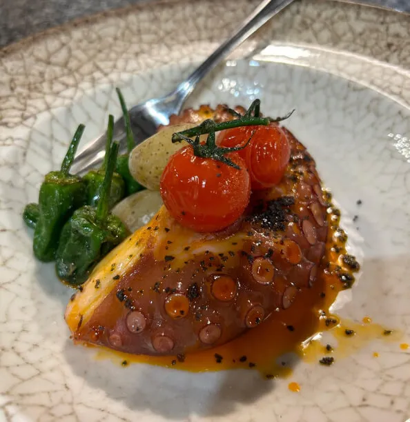 Un plato de pulpo con pimientos y tomates de la huerta sobre una mesa.