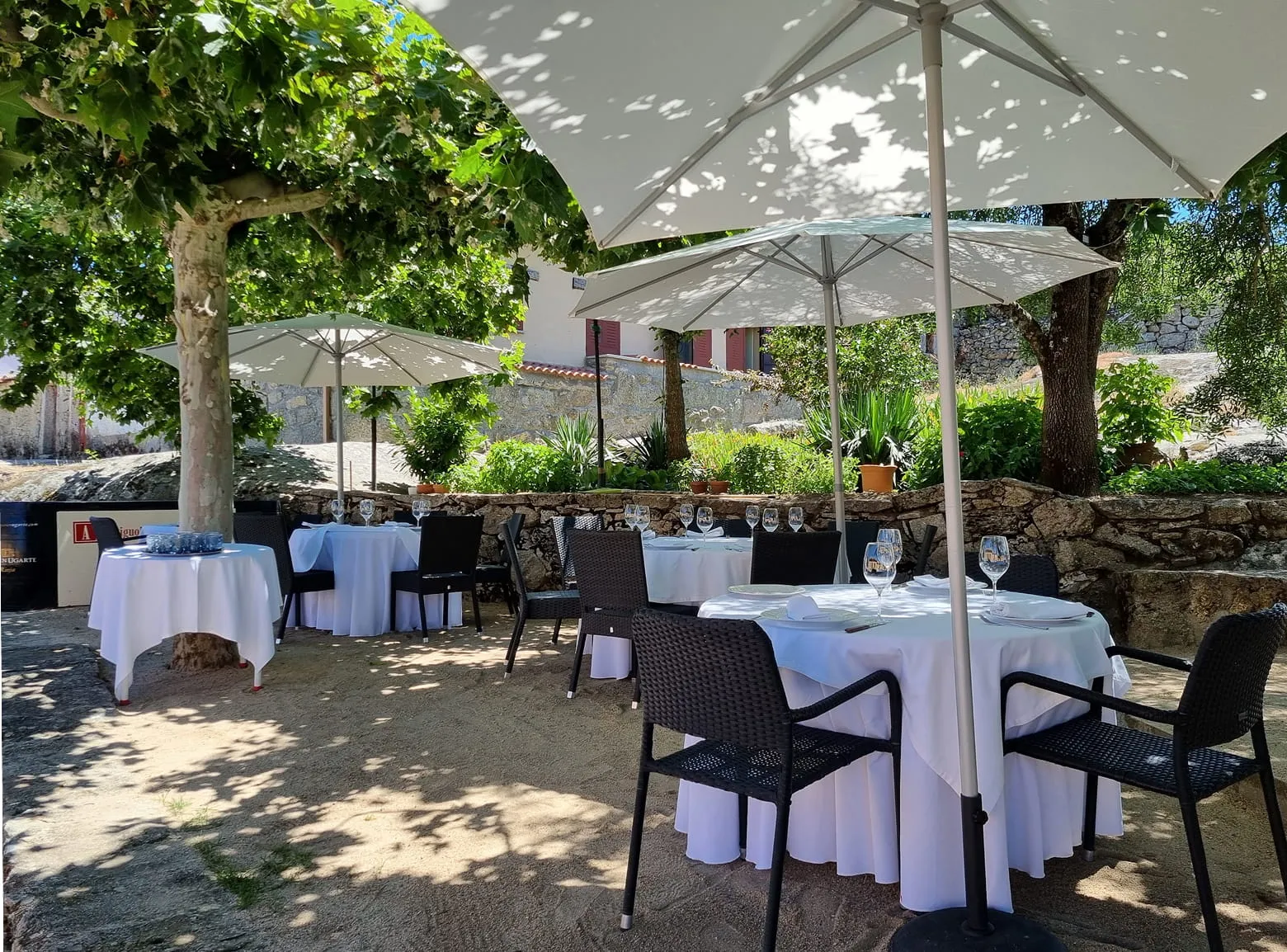 Terraza exterior del restaurante Antiguo Mesón Fuentebuena con mesas bajo los árboles.
